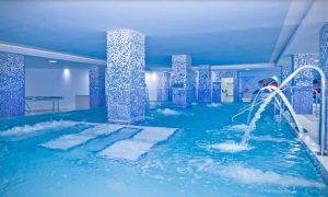 Experimente el lujo en la piscina cubierta del Hotel Gala en Tenerife, con columnas de mosaico azul, chorros de agua y plataformas sumergidas. Ideal para una sesión de spa en pareja gracias a su diseño espacioso y moderno. - ForTwo - Planes para parejas