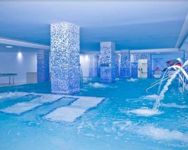 Experimente el lujo en la piscina cubierta del Hotel Gala en Tenerife, con columnas de mosaico azul, chorros de agua y plataformas sumergidas. Ideal para una sesión de spa en pareja gracias a su diseño espacioso y moderno. - ForTwo - Planes para parejas