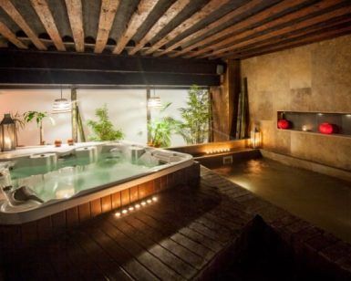 Una acogedora sala de spa con jacuzzi, iluminación ambiental y exuberante vegetación refleja el estilo del Spa y masaje a lo japonés + menú de tapas en Madrid. Faroles rojos decorativos en una pared de piedra aportan un toque elegante. - ForTwo - Planes para parejas