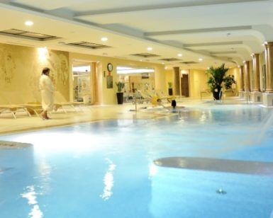 El Circuito Relax del Auditorio Beatriz Toledo cuenta con una tranquila piscina interior con tumbonas, una persona en bata y un nadador rodeados de una elegante iluminación y decoración. - ForTwo - Planes para parejas