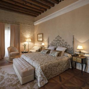 Descubra la elegancia de La suite perfecta de la mansión La Casa 1800 en Sevilla, con su cama decorativa, sus acogedores sillones y su suave iluminación. El techo con vigas de madera realza la majestuosidad de este elegante refugio. - ForTwo - Planes para parejas