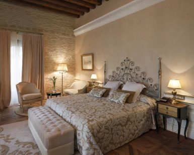 Descubra la elegancia de La suite perfecta de la mansión La Casa 1800 en Sevilla, con su cama decorativa, sus acogedores sillones y su suave iluminación. El techo con vigas de madera realza la majestuosidad de este elegante refugio. - ForTwo - Planes para parejas