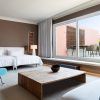 Descubra la comodidad de nuestra Suite Grand Terrace, la comodidad hecha habitación (Barcelona), con dos camas, una mesa de madera y una silla azul. Disfrute de la vista a través de un amplio ventanal que da a una terraza con acogedores asientos. - ForTwo - Planes para parejas