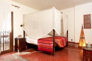 Un acogedor dormitorio con cama con dosel, manta colorida, muebles de madera y linterna decorativa sobre el suelo de baldosas rojas ofrece el ambiente perfecto para quienes buscan Suites románticas con jacuzzi en Alcoba del Rey de Sevilla (Sevilla). - ForTwo - Planes para parejas