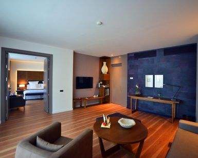 Experimente La suite presidencial del Hotel Barceló Sevilla Renacimiento en Sevilla: un refugio espacioso y moderno que cuenta con un dormitorio, sala de estar, elegantes pisos de madera y una llamativa pared de acento oscuro, que combina a la perfección comodidad y estilo. - ForTwo - Planes para parejas