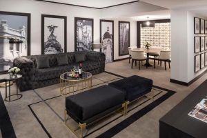 Descubra la elegancia de la Suite presidencial en el hotel Meliá Castilla (Madrid), que cuenta con una refinada sala de estar con un sofá negro, una mesa redonda y llamativas fotografías de la ciudad en blanco y negro que complementan a la perfección el elegante comedor. - ForTwo - Planes para parejas