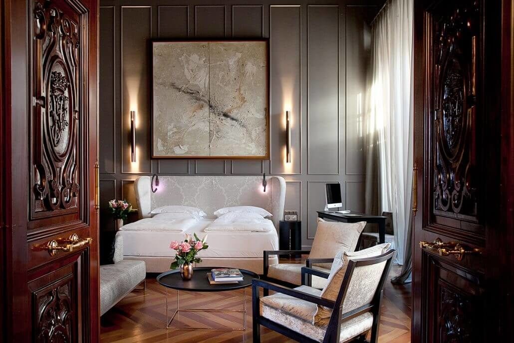 Descubra la elegancia de nuestras Suites únicas en el Hotel Palacio De Villapanés (Sevilla), con cama de matrimonio, acogedores sillones, puertas decorativas de madera y un impresionante cuadro abstracto de gran tamaño. - ForTwo - Planes para parejas