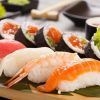 Cenita de sushi para 2 personas en Sushi Volcán (Bilbao) cuenta con una variedad de nigiris y rolls con pescado crudo y camarones, servidos en una bandeja de madera con hojas verdes, trayendo la vibrante escena culinaria de Bilbao a tu mesa. - ForTwo - Planes para parejas
