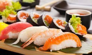 Cenita de sushi para 2 personas en Sushi Volcán (Bilbao) cuenta con una variedad de nigiris y rolls con pescado crudo y camarones, servidos en una bandeja de madera con hojas verdes, trayendo la vibrante escena culinaria de Bilbao a tu mesa. - ForTwo - Planes para parejas