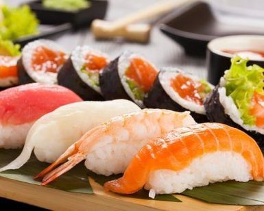 Cenita de sushi para 2 personas en Sushi Volcán (Bilbao) cuenta con una variedad de nigiris y rolls con pescado crudo y camarones, servidos en una bandeja de madera con hojas verdes, trayendo la vibrante escena culinaria de Bilbao a tu mesa. - ForTwo - Planes para parejas
