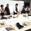 Personas con delantales observan a un chef en el mostrador de la cocina, mostrando habilidades culinarias durante una vibrante experiencia de Taller de Cocina en Illa Diagonal en Barcelona. - ForTwo - Planes para parejas