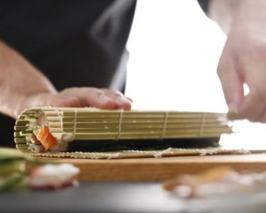 Primer plano de unas manos enrollando sushi con destreza con una estera de bambú, capturando la esencia de la auténtica preparación de sushi en el Taller de preparación de sushi (Madrid). - ForTwo - Planes para parejas