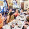 Gente disfrutando de un "Tour de tapas por Barcelona" en un animado restaurante, cenando en una mesa larga con bebidas, rodeados de una decoración colorida que recuerda a una vibrante noche de Barcelona. - ForTwo - Planes para parejas