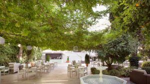 Junto a una exuberante vegetación, esta lujosa cafetería al aire libre en el Hotel Palacio de los Patos ofrece serenas vistas a la fuente y un sofisticado bar, que encarna el tranquilo ambiente de spa de la "Escapada de lujo en el hotel Palacio de los Patos con spa incluido (Granada). - ForTwo - Planes para parejas