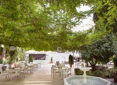 Junto a una exuberante vegetación, esta lujosa cafetería al aire libre en el Hotel Palacio de los Patos ofrece serenas vistas a la fuente y un sofisticado bar, que encarna el tranquilo ambiente de spa de la "Escapada de lujo en el hotel Palacio de los Patos con spa incluido (Granada). - ForTwo - Planes para parejas