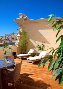 La Suite con terraza y Spa del Hotel Boutique Hurso (Madrid) cuenta con dos tumbonas, una mesa de mimbre y exuberantes plantas bajo un cielo azul despejado. Disfrute hoy de su oasis de serenidad. - ForTwo - Planes para parejas