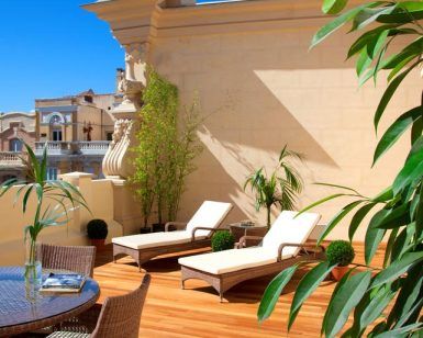 La Suite con terraza y Spa del Hotel Boutique Hurso (Madrid) cuenta con dos tumbonas, una mesa de mimbre y exuberantes plantas bajo un cielo azul despejado. Disfrute hoy de su oasis de serenidad. - ForTwo - Planes para parejas