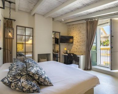 Disfrute de una acogedora habitación en el Hotel Torre del Canónigo (Ibiza), decorada con detalles en blanco, almohadas estampadas, televisor y acceso al balcón. Disfrute del encanto de las vigas de madera rústicas y los detalles de piedra en las paredes, creando un ambiente acogedor. - ForTwo - Planes para parejas