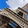 Vista en ángulo bajo de la Torre Eiffel contra un cielo azul nublado en París, mostrando su grandeza con un pase "Visita la Torre Eiffel sin hacer cola (París)". - ForTwo - Planes para parejas