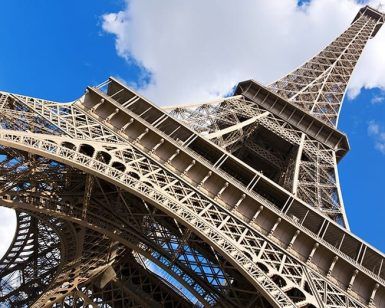 Vista en ángulo bajo de la Torre Eiffel contra un cielo azul nublado en París, mostrando su grandeza con un pase "Visita la Torre Eiffel sin hacer cola (París)". - ForTwo - Planes para parejas