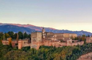 Encaramada en una colina, la fortaleza presume de majestuosas torres y murallas que contrastan con impresionantes montañas bajo un cielo despejado. Experimente la grandeza de este monumento con la "Visita privada exclusiva para parejas con entradas y guía oficial por la Alhambra". - ForTwo - Planes para parejas