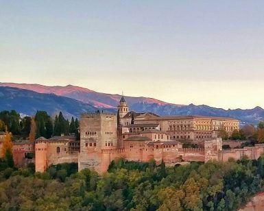 Encaramada en una colina, la fortaleza presume de majestuosas torres y murallas que contrastan con impresionantes montañas bajo un cielo despejado. Experimente la grandeza de este monumento con la "Visita privada exclusiva para parejas con entradas y guía oficial por la Alhambra". - ForTwo - Planes para parejas