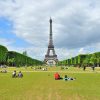 La gente se relaja en el césped con la Torre Eiffel de fondo bajo un cielo parcialmente nublado, perfecto para descansar después de una Visitada guiada por París gratis. - ForTwo - Planes para parejas