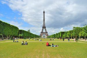 La gente se relaja en el césped con la Torre Eiffel de fondo bajo un cielo parcialmente nublado, perfecto para descansar después de una Visitada guiada por París gratis. - ForTwo - Planes para parejas