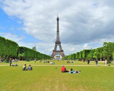 La gente se relaja en el césped con la Torre Eiffel de fondo bajo un cielo parcialmente nublado, perfecto para descansar después de una Visitada guiada por París gratis. - ForTwo - Planes para parejas