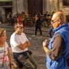 Tres personas charlan en una calle soleada, mientras otras están sentadas en mesas al aire libre al fondo, quizás comentando su reciente "Tour Guiado en Granada por Albaicín y Sacromonte" o planeando una aventura por el histórico barrio del Albaicín. - ForTwo - Planes para parejas