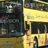 Un autobús amarillo brillante de dos pisos con la etiqueta BUSVISION recorre Madrid. El "Tour panorámico por Madrid en autobús de lujo" ofrece a los pasajeros vistas panorámicas desde el piso superior, haciendo que cada viaje sea inolvidable. - ForTwo - Planes para parejas