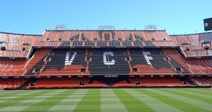Las gradas del estadio exhiben grandes letras VCF con filas de asientos rojos y negros sobre el vibrante campo verde. Disfruta de esta icónica vista durante el tour Visita Mestalla con el Mestalla Forever en el famoso estadio del Valencia. - ForTwo - Planes para parejas