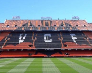 Las gradas del estadio exhiben grandes letras VCF con filas de asientos rojos y negros sobre el vibrante campo verde. Disfruta de esta icónica vista durante el tour Visita Mestalla con el Mestalla Forever en el famoso estadio del Valencia. - ForTwo - Planes para parejas