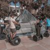 La gente que realiza la "Ruta en segway por Málaga" se desliza alrededor de una pirámide de cristal en un parque soleado con árboles al fondo. - ForTwo - Planes para parejas