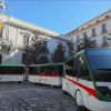 Tres autobuses eléctricos en verde y blanco, estacionados en una plaza con edificios históricos detrás, haciendo eco de las Entradas para Tren turístico en Granada, combinan la elegancia moderna con el encanto atemporal de Granada. - ForTwo - Planes para parejas