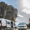 Dos Escapada romántica en furgoneta camperizada con Vantrip (Barcelona) están aparcadas junto a formaciones rocosas; un escalador escala la roca bajo un cielo soleado con nubes dispersas, ideal para este emocionante vantrip. - ForTwo - Planes para parejas
