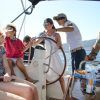 La gente disfruta de un día soleado en una "Experiencia en velero en Barcelona + Vermú", con una persona al volante y otros relajándose en la cubierta, bebiendo Vermú. - ForTwo - Planes para parejas