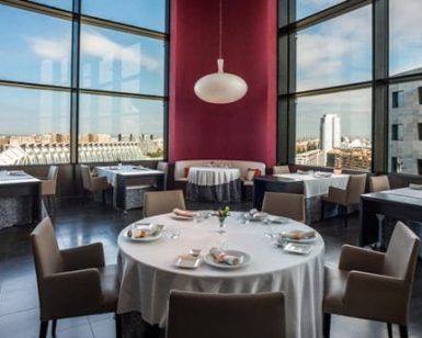 Restaurante Vertical en Valencia ofrece una elegante experiencia gastronómica con mesas redondas vestidas con manteles blancos, grandes ventanales que ofrecen vistas panorámicas de la ciudad y una decoración moderna que añade sofisticación. - ForTwo - Planes para parejas