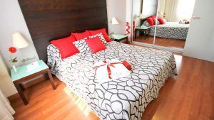 Cree un retiro inspirado en Sevilla con elementos modernos y elegantes, como una colcha estampada, almohadas rojas y puertas de armario con espejos, ideal después de disfrutar de "Escapada con desayuno, bañera de hidromasaje y entradas al Gran Casino Aljarafe (Sevilla). - ForTwo - Planes para parejas