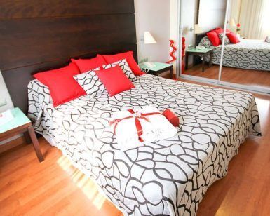 Cree un retiro inspirado en Sevilla con elementos modernos y elegantes, como una colcha estampada, almohadas rojas y puertas de armario con espejos, ideal después de disfrutar de "Escapada con desayuno, bañera de hidromasaje y entradas al Gran Casino Aljarafe (Sevilla). - ForTwo - Planes para parejas