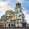 La pintoresca catedral, con su cúpula verde y dorada, se alza majestuosa contra un atardecer parcialmente nublado, capturando el patrimonio arquitectónico celebrado en "Descubre Rumanía y Bulgaria". - ForTwo - Planes para parejas