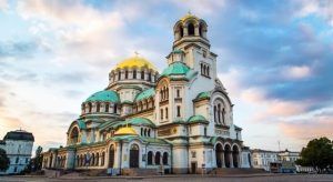 La pintoresca catedral, con su cúpula verde y dorada, se alza majestuosa contra un atardecer parcialmente nublado, capturando el patrimonio arquitectónico celebrado en "Descubre Rumanía y Bulgaria". - ForTwo - Planes para parejas