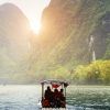 Un barco se desliza por un río con pasajeros bajo un cielo brumoso, enclavado entre altas y verdes montañas que recuerdan a la China clásica y a Hong Kong. - ForTwo - Planes para parejas