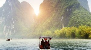 Un barco se desliza por un río con pasajeros bajo un cielo brumoso, enclavado entre altas y verdes montañas que recuerdan a la China clásica y a Hong Kong. - ForTwo - Planes para parejas