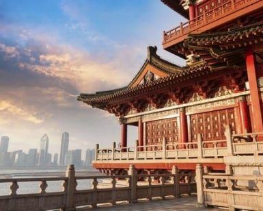 La escena presenta un edificio tradicional chino de "Viaje a China: de Pekín a Shanghai", con vistas al vibrante horizonte de Shanghai al atardecer, con detalles ornamentados bajo un cielo nublado. - ForTwo - Planes para parejas
