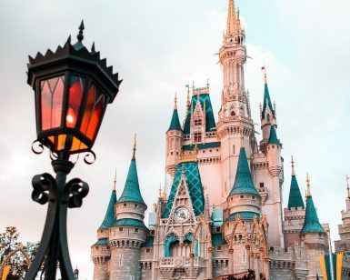Una linterna antigua enmarca un castillo adornado con agujas azules bajo un cielo nublado de Europa, capturando el encanto de un "Viaje sorpresa en pareja a un parque de atracciones en Europa". - ForTwo - Planes para parejas