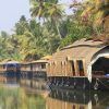 Casas flotantes en un río tranquilo en el sur de la India, rodeadas de exuberantes palmeras y vegetación bajo un cielo despejado, proporcionan el escenario ideal para un Viaje por el sur de la India por 10 días. - ForTwo - Planes para parejas