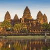Angkor Wat, una joya de Camboya, se refleja en un estanque tranquilo bajo un cielo despejado y palmeras, encapsulando el encanto que se encuentra en "Vietnam y Camboya: 12 noches de esencia pura asiática". - ForTwo - Planes para parejas