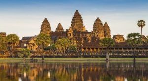 Angkor Wat, una joya de Camboya, se refleja en un estanque tranquilo bajo un cielo despejado y palmeras, encapsulando el encanto que se encuentra en "Vietnam y Camboya: 12 noches de esencia pura asiática". - ForTwo - Planes para parejas