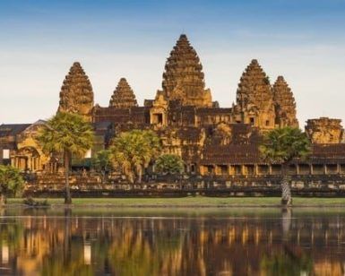 Angkor Wat, una joya de Camboya, se refleja en un estanque tranquilo bajo un cielo despejado y palmeras, encapsulando el encanto que se encuentra en "Vietnam y Camboya: 12 noches de esencia pura asiática". - ForTwo - Planes para parejas